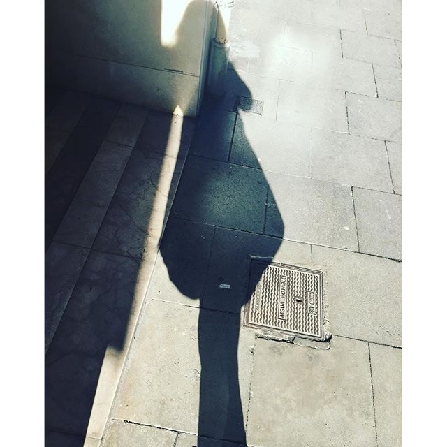 Sombra alargada de una persona proyectada sobre un pavimento de baldosas, junto a unas escaleras