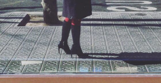 Una mujer con botas, vista de rodillas para abajo, en el bordillo de una acera