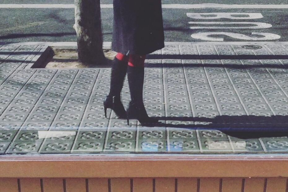 Una mujer con botas, vista de rodillas para abajo, en el bordillo de una acera
