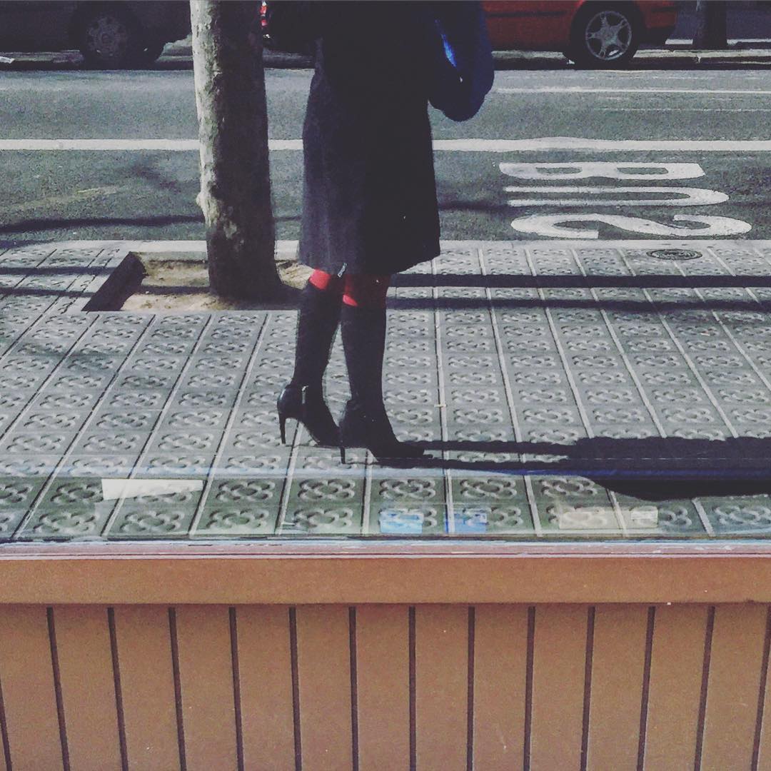Una mujer con botas, vista de rodillas para abajo, en el bordillo de una acera