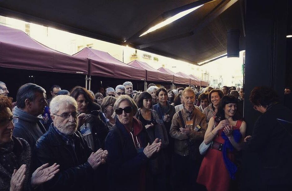 Multitud de escritores y público aplaudiendo bajo un toldo en la Llibreria El Cucut