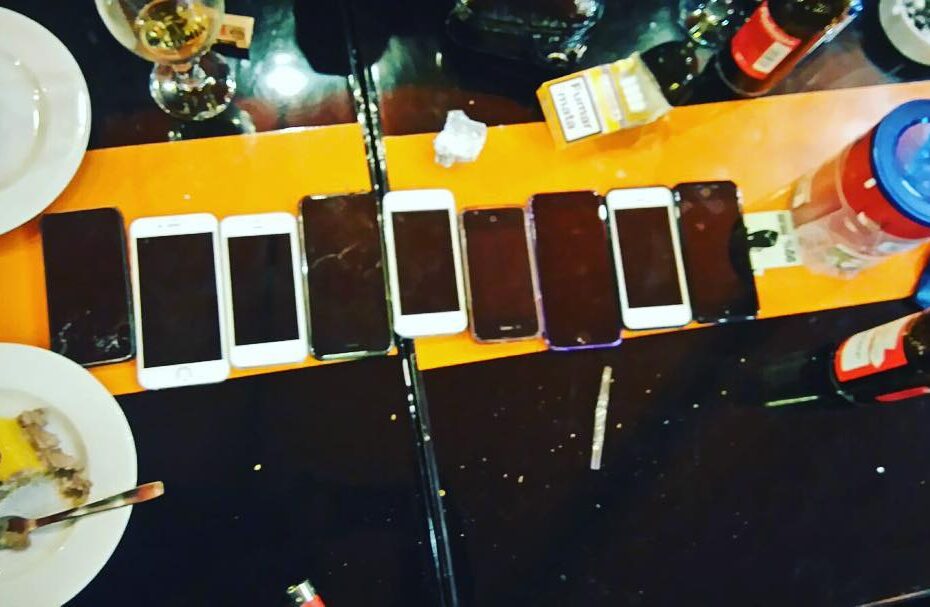 Ocho teléfonos móviles alineados sobre una mesa naranja de bar, entre platos de postre