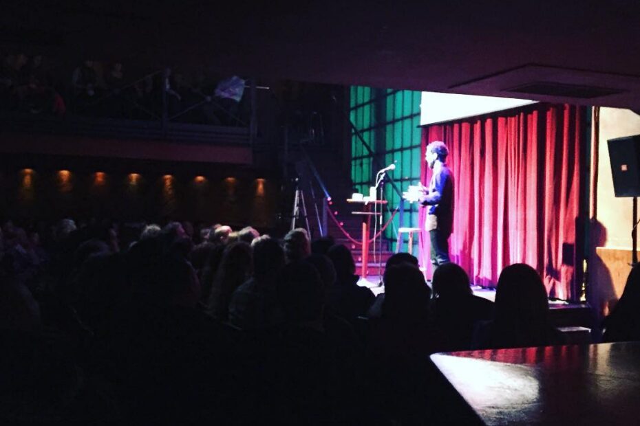 Escenario de la sala Luz de Gas, de Barcelona, con una persona ante el micrófono y el público en penumbra