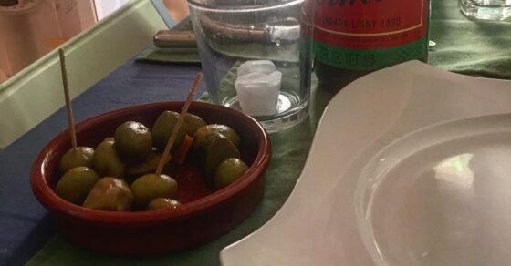 Bol d’olives verdes amb escuradents, una ampolla de vermut i plats buits sobre una estovalla verda