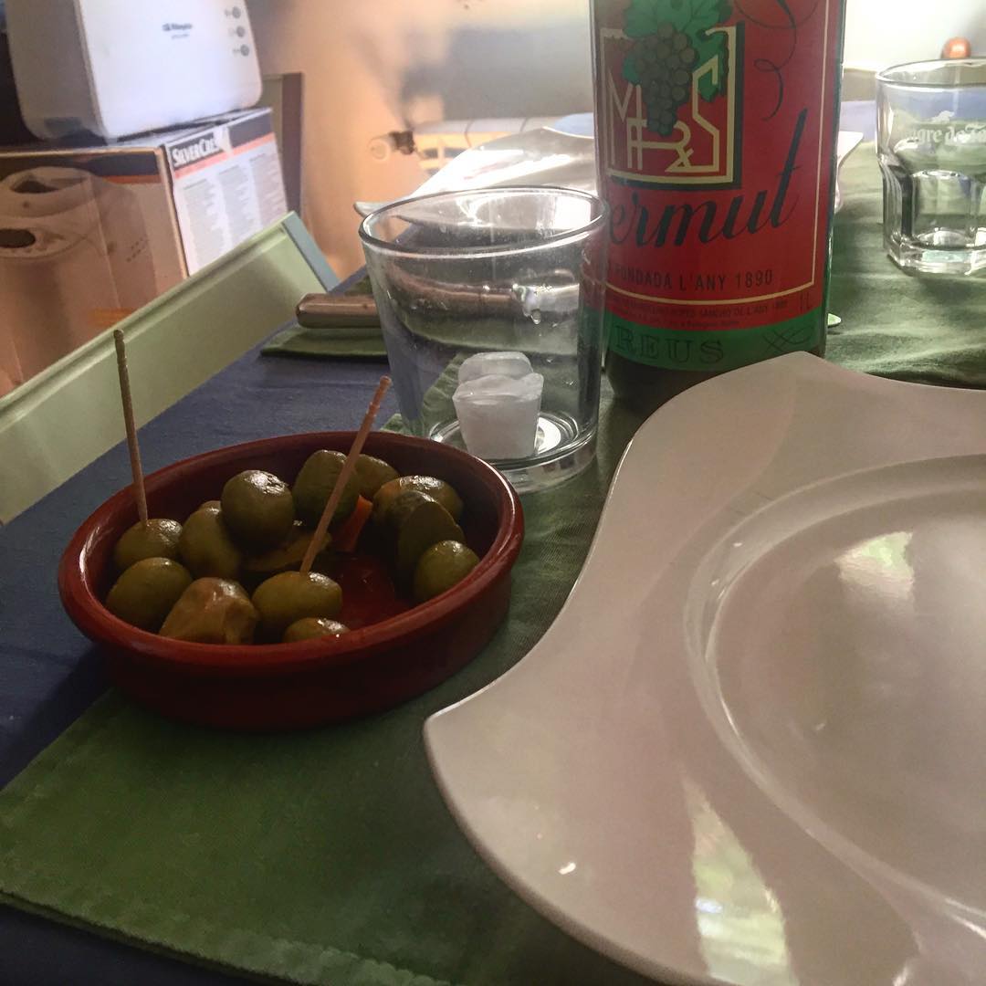 Bol d’olives verdes amb escuradents, una ampolla de vermut i plats buits sobre una estovalla verda