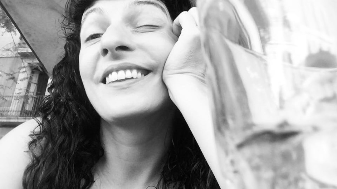 Roser Amills sonriendo con los ojos cerrados y la mano en la mejilla, en blanco y negro