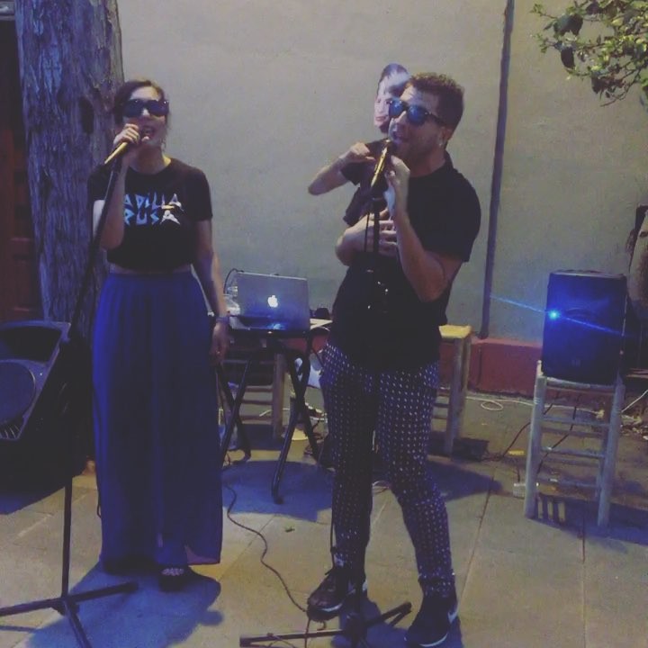 Tània Lozano y Víctor Fernández Clares, con gafas de sol, cantando en un patio con un portátil y altavoces