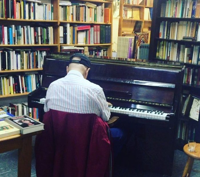 Josep Batlló toca el piano de espaldas en la librería Taifa, rodeado de estanterías de libros