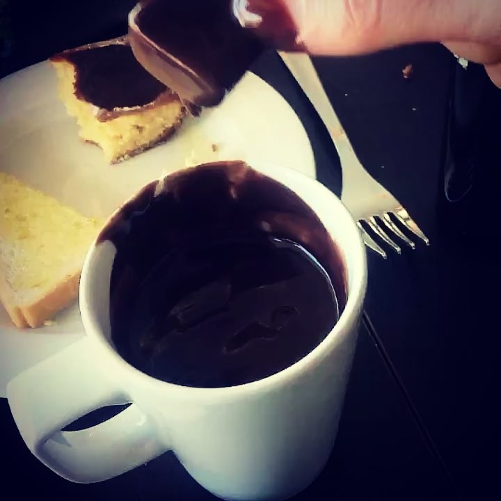 Una taza de chocolate caliente junto a un plato con bizcocho, mientras una mano vierte más chocolate, el 18 de noviembre de 2017