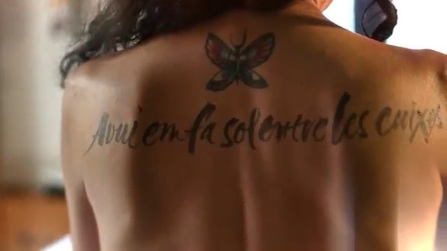 Espalda de Roser Amills con el verso «Avui em fa sol entre les cuixes» caligrafiado y una mariposa dibujada
