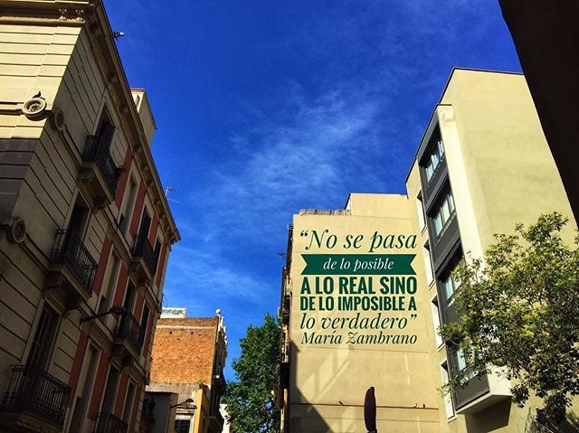 Mural en la fachada de un edificio con la frase «No se pasa de lo posible a lo real, sino de lo imposible a lo verdadero», de María Zambrano, bajo un cielo azul