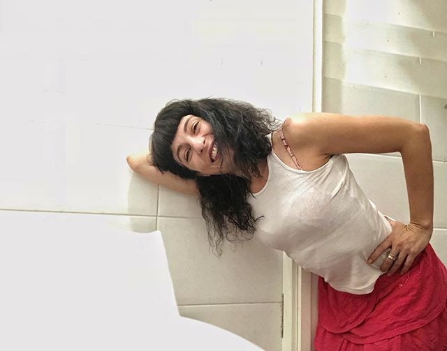 Roser Amills, con camiseta de tirantes blanca y falda roja, apoyada en una pared blanca y sonriendo