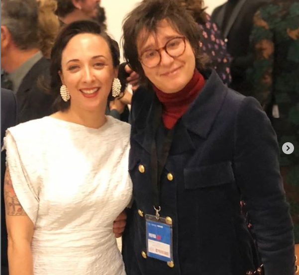 Bea Castelló junto a otra mujer, con acreditación, en un acto con público