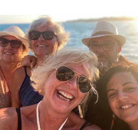 Selfi de Carmen Linares con varias amigas y un amigo, con gafas de sol, al atardecer junto al mar
