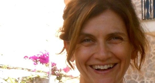 Retrato de la novelista Mar Mella sonriente al aire libre, con buganvillas al fondo