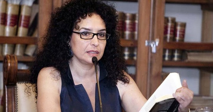 Una dona amb ulleres i cabell arrissat llegeix davant d'un micròfon