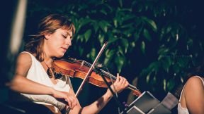 Violeta Paulina toca el violín con una camiseta blanca, ante un fondo de hojas