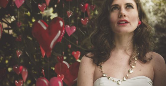 Ivana Berenstein, con vestido blanco, mira hacia arriba ante una cortina de corazones rojos