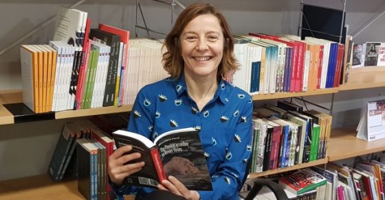 Izaskun Arretxe sonríe con un libro abierto ante las estanterías de una librería