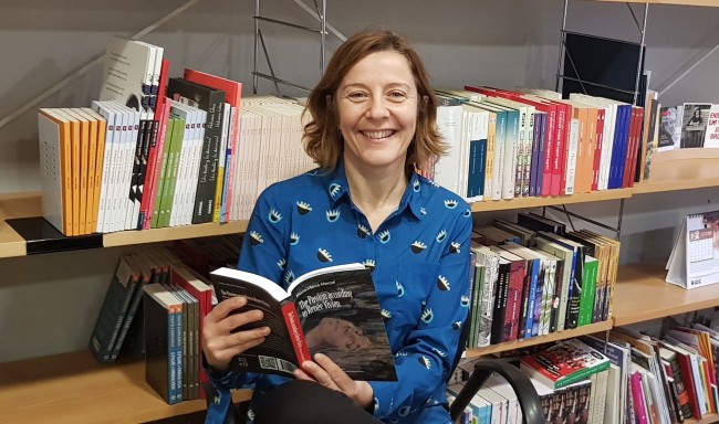 Izaskun Arretxe sonríe con un libro abierto ante las estanterías de una librería