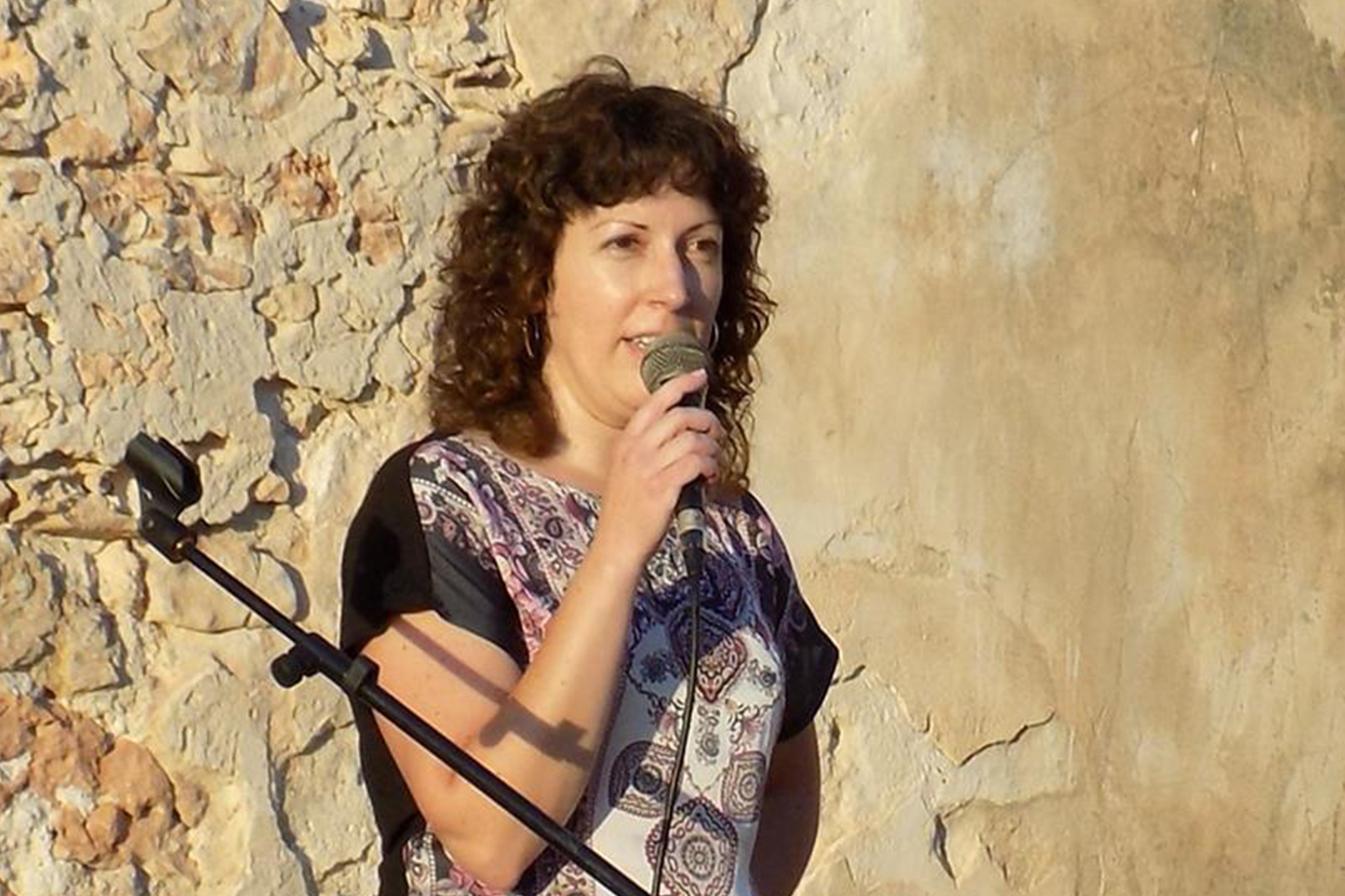 Maria Teresa Ferrer habla ante un micrófono junto a un muro de piedra