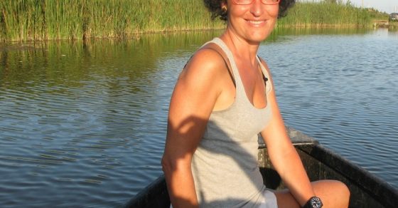 Montse Ferrer, con gafas rojas, sentada en una barca en un canal entre cañaverales
