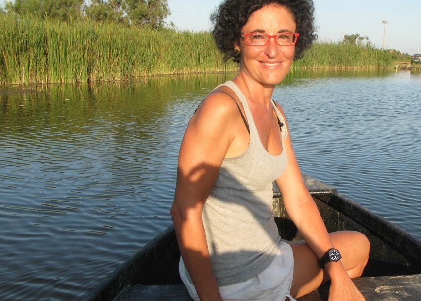 Montse Ferrer, con gafas rojas, sentada en una barca en un canal entre cañaverales