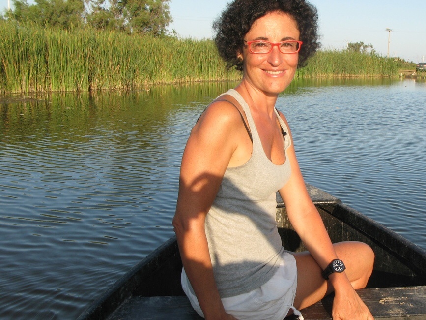 Montse Ferrer, con gafas rojas, sentada en una barca en un canal entre cañaverales