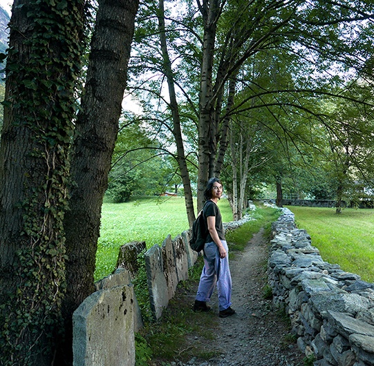 Una mujer camina por un sendero junto a un muro de piedra en un bosque
