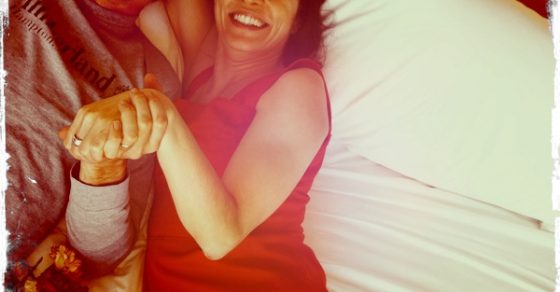 Roser Amills, con vestido rojo, y Jordi Play tumbados en una cama con rosas rojas