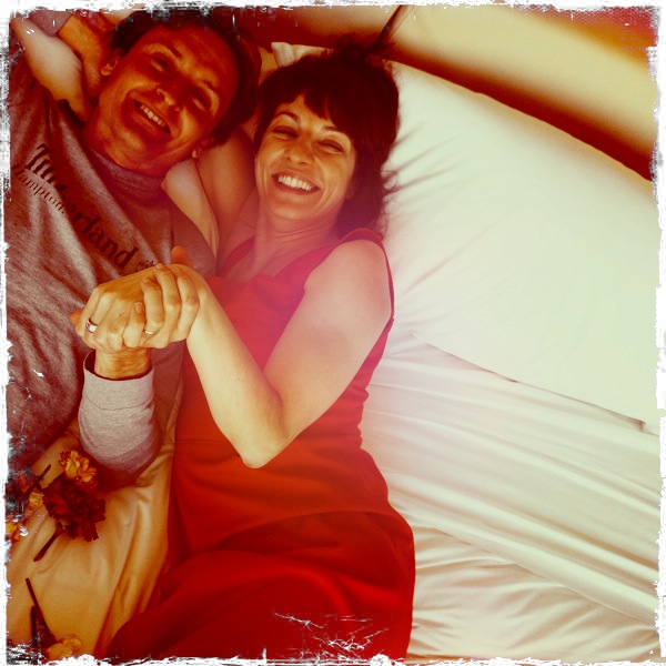 Roser Amills, con vestido rojo, y Jordi Play tumbados en una cama con rosas rojas