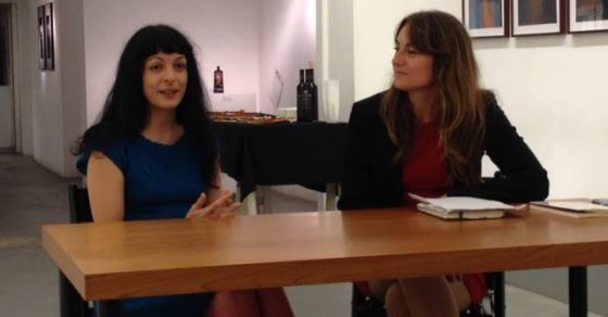 Roser Amills y Maria Coloma Mairata conversan sentadas a una mesa en una sala con cuadros