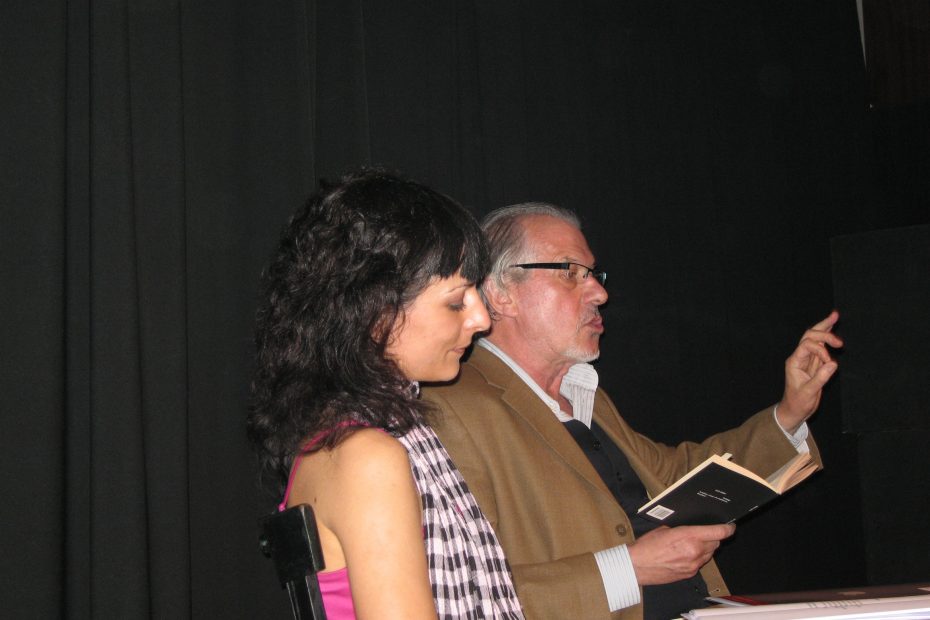 Iván Tubau lee y gesticula sentado junto a Roser Amills en un escenario oscuro