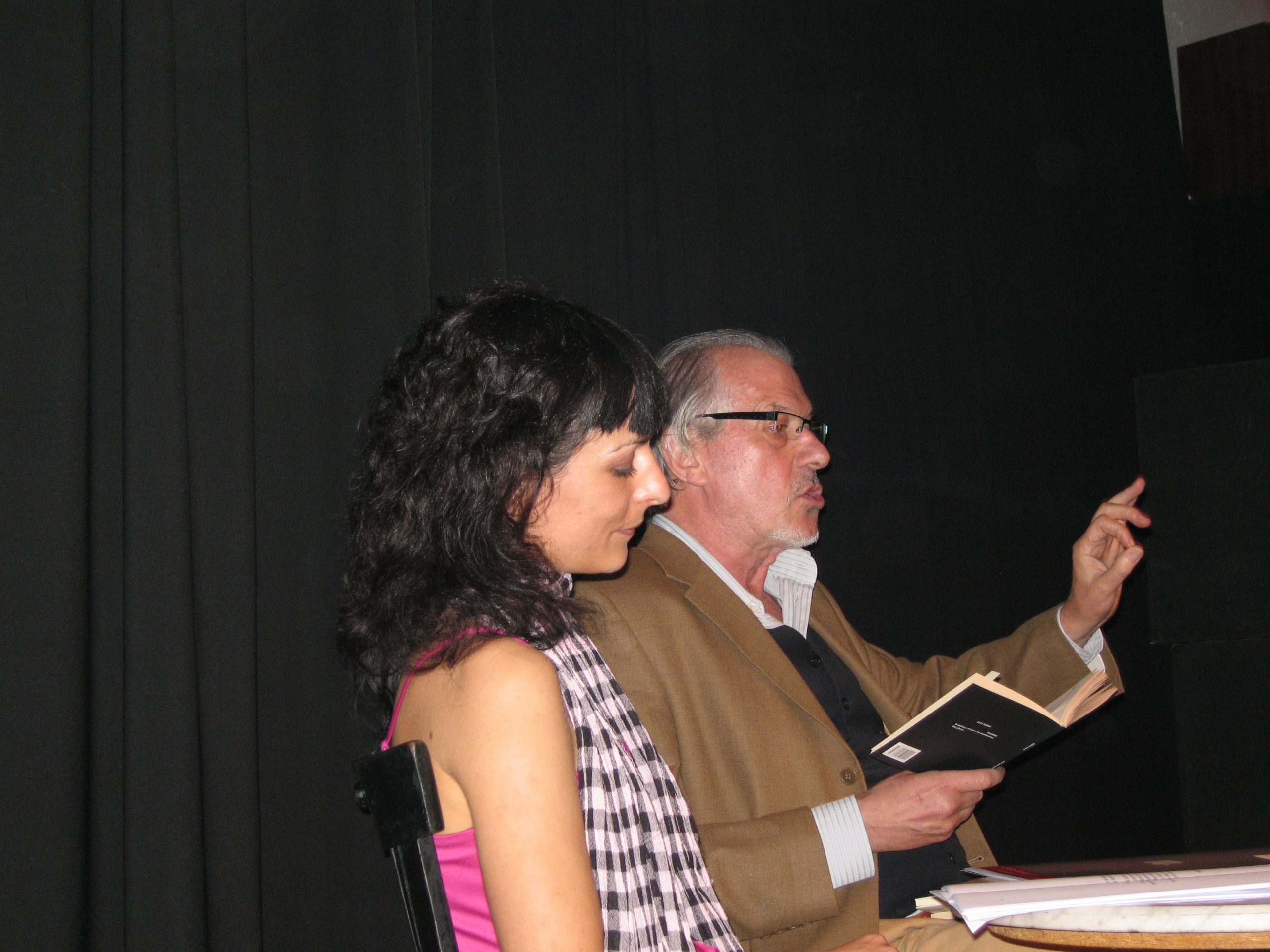 Iván Tubau lee y gesticula sentado junto a Roser Amills en un escenario oscuro