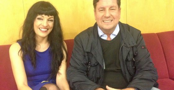 Roser Amills, con vestido azul, y Eduard Ruiz Castañé sentados en un sofá rojo ante el rótulo de Catalunya Ràdio