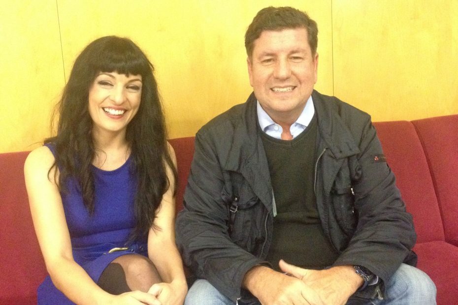 Roser Amills, con vestido azul, y Eduard Ruiz Castañé sentados en un sofá rojo ante el rótulo de Catalunya Ràdio