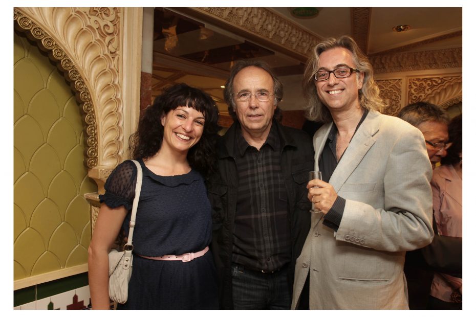 Roser Amills, Joan Manuel Serrat y Víctor Amela, sonrientes, posando juntos ante un arco ornamentado