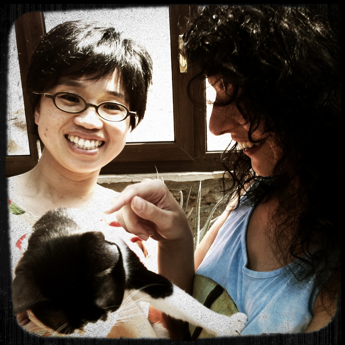 Primer plano de Naoko, con gafas y pelo corto, sonriendo junto a Roser Amills y un gato