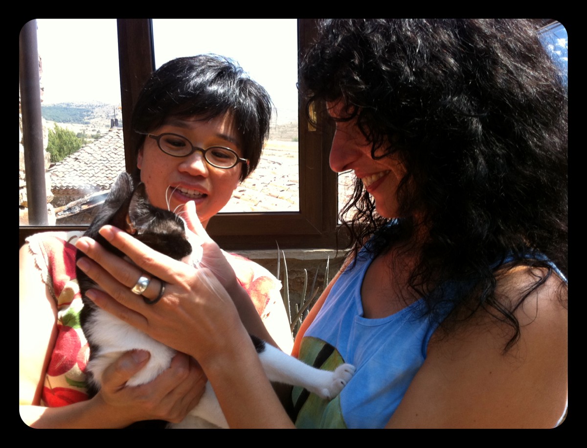 Naoko con un gato en brazos y Roser Amills a su lado junto a una ventana luminosa
