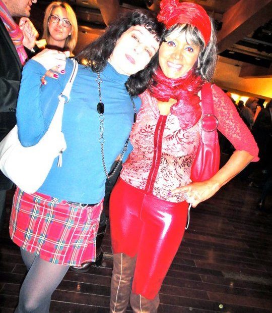 Roser Amills, con falda escocesa, y Regina do Santos, con pantalón rojo de charol y gorro rojo, en una fiesta