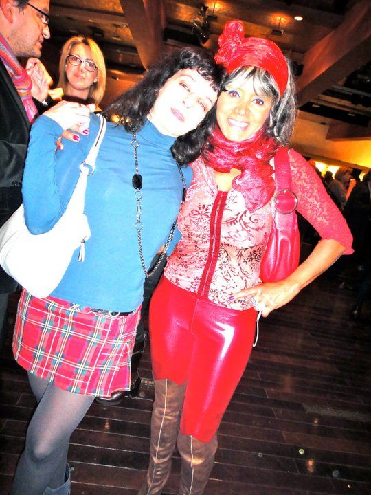 Roser Amills, con falda escocesa, y Regina do Santos, con pantalón rojo de charol y gorro rojo, en una fiesta