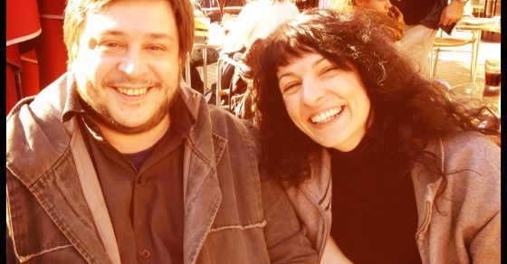 Roser Amills y el escritor Hernán Casciari, con cazadora marrón, sonríen en una terraza soleada