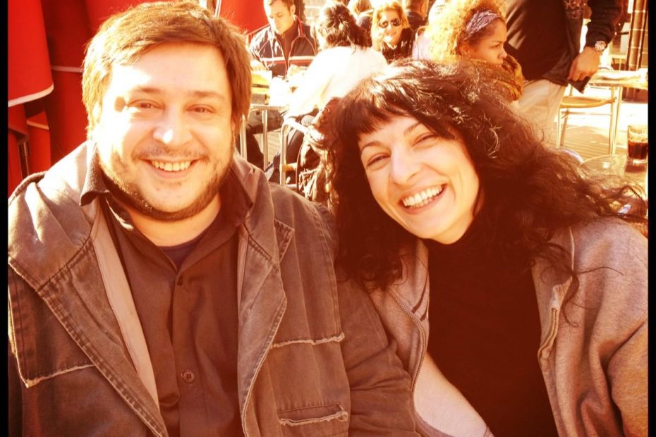 Roser Amills y el escritor Hernán Casciari, con cazadora marrón, sonríen en una terraza soleada