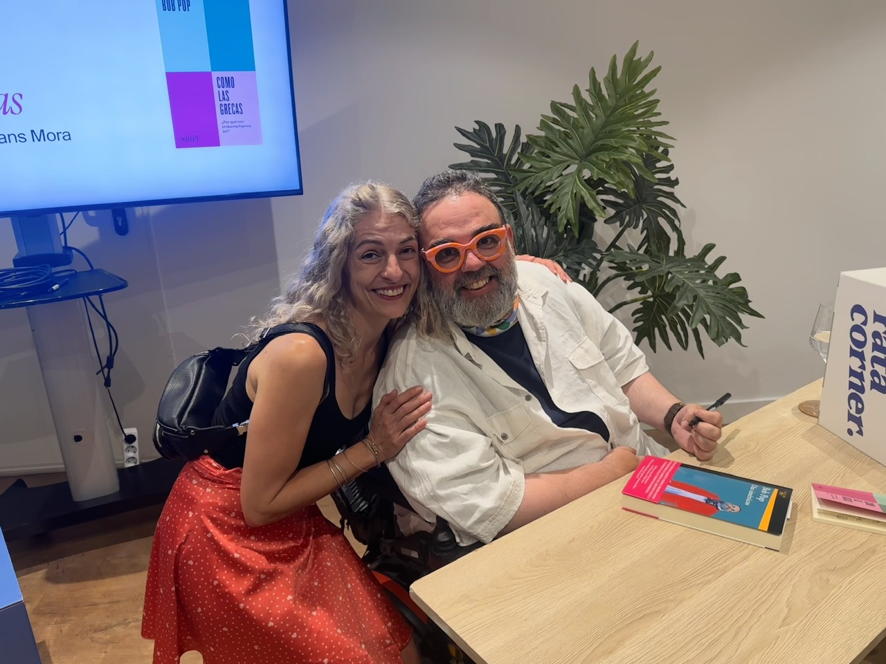 Roser Amills y Bob Pop, con gafas rojas, posan abrazados en la mesa de firmas