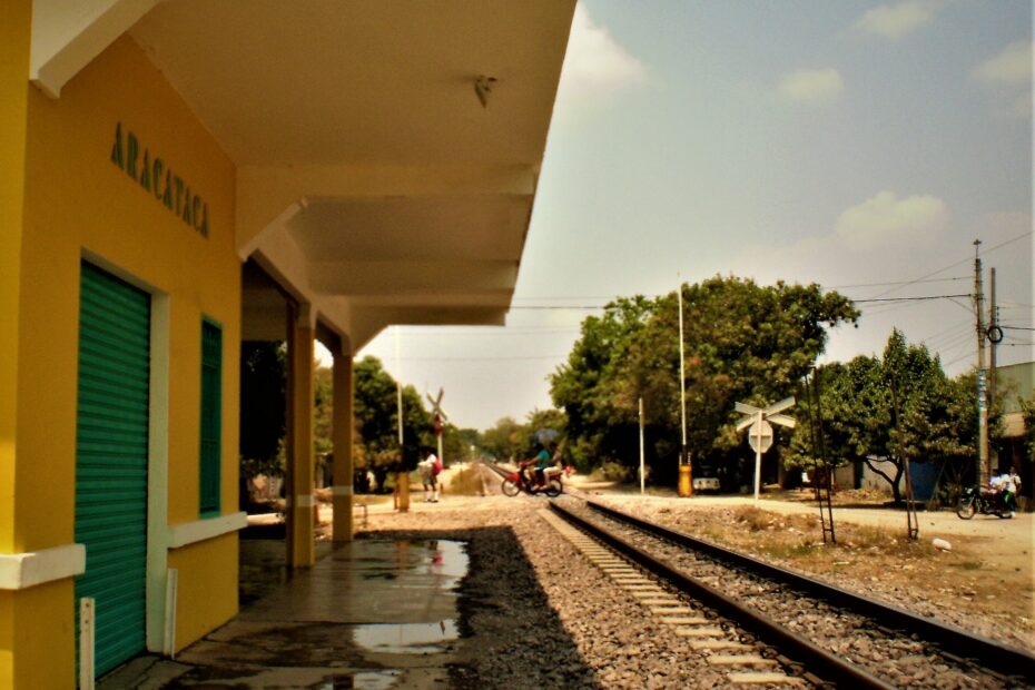 Andén amarillo de la estación de Aracataca, con el nombre del pueblo en la fachada y las vías del tren que se pierden entre árboles