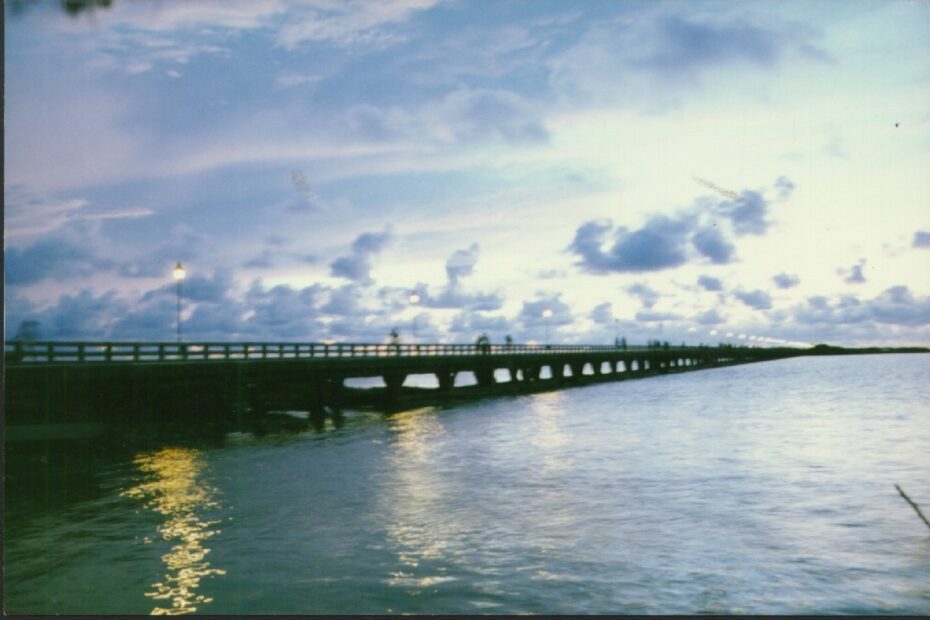 El largo muelle de Puerto Colombia adentrándose en el mar al atardecer, con farolas encendidas y nubes violáceas