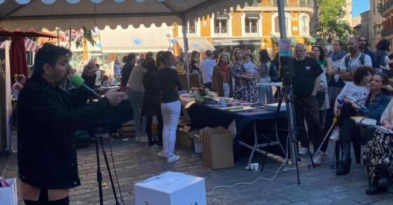 Grup de persones davant la parada d'Ona Mediterrània i dBalears sota una carpa verda a la plaça de Cort, a Palma