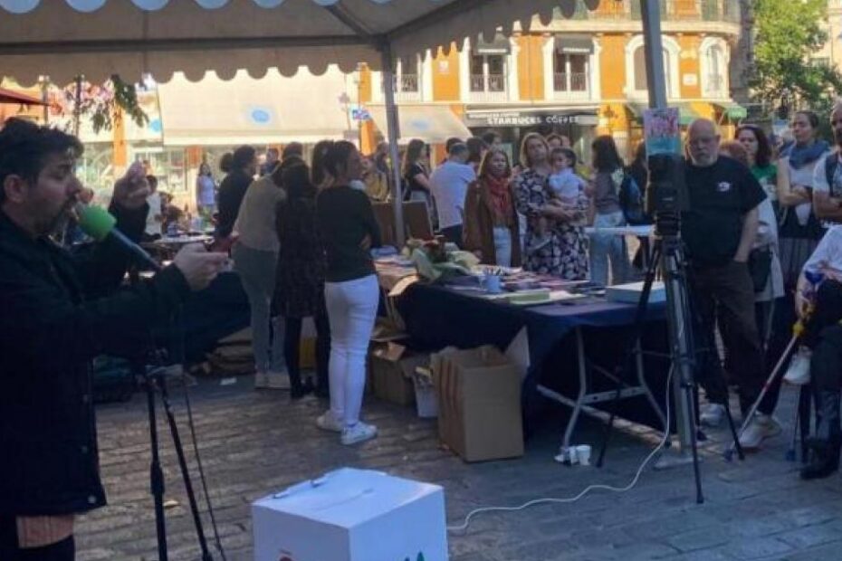 Grup de persones davant la parada d'Ona Mediterrània i dBalears sota una carpa verda a la plaça de Cort, a Palma