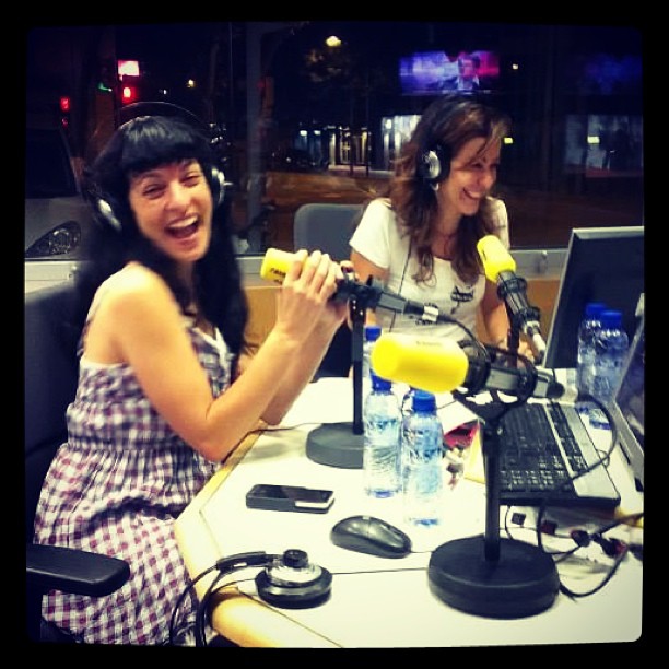 Roser Amills riendo ante un micrófono amarillo en el estudio de radio, con otra mujer al fondo