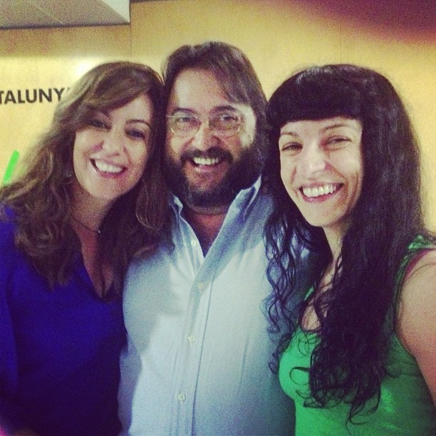 Roser Amills sonríe junto a una mujer y un hombre con barba ante un cartel de Catalunya Ràdio